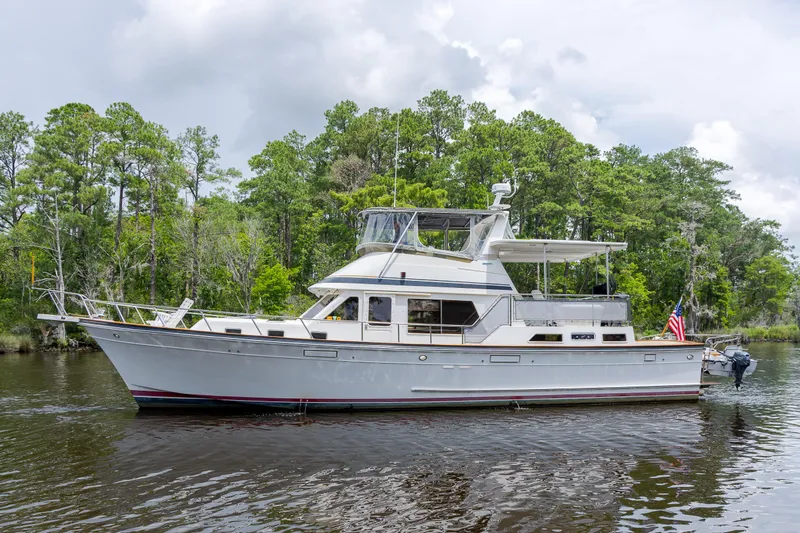  Yacht Photos Pics 1989 Offshore Yachts 48 Yachtfisher cruising on a serene river, surrounded by lush greenery.