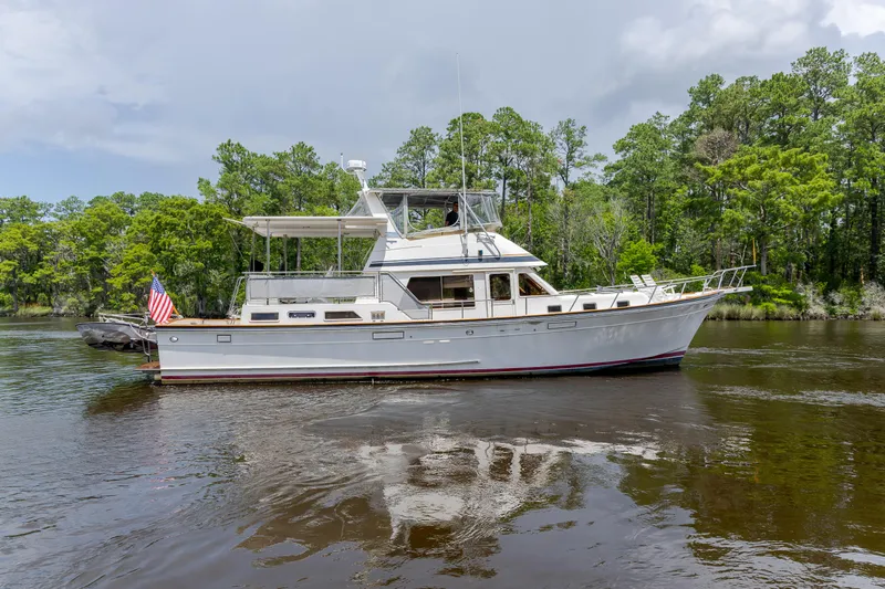  Yacht Photos Pics 1989 Offshore Yachts 48 Yachtfisher cruising on a serene river with lush green trees.