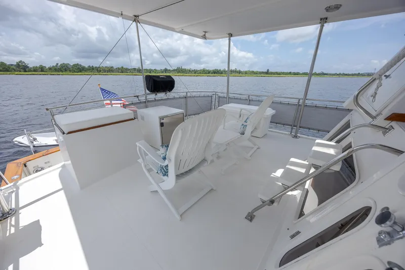 Yacht Photos Pics 1989 Offshore Yachts 48 Yachtfisher deck with chairs, overlooking serene water and lush greenery.
