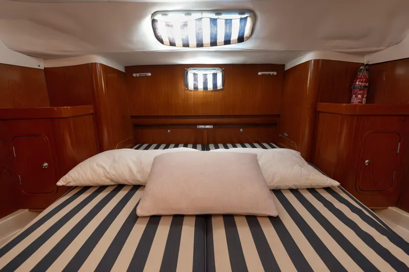  Yacht Photos Pics Cozy cabin interior of 1999 Beneteau Oceanis 44 CC with striped bedding and wooden finish.