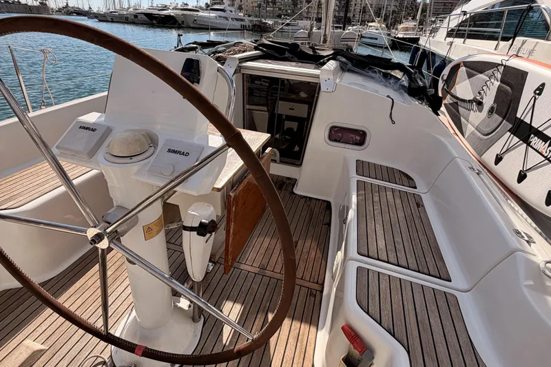  Yacht Photos Pics Beneteau Oceanis 370 sailboat cockpit with wooden deck, steering wheel, and marina view.