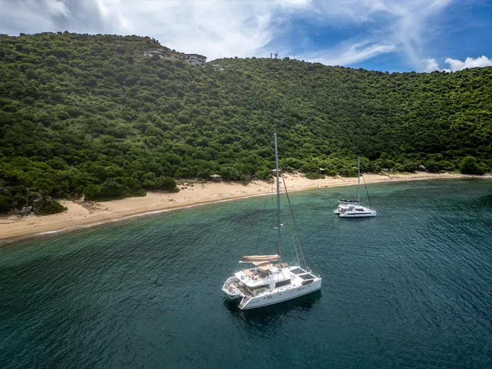 Cascadia 2 Yacht Photos Pics Two Lagoon 560 catamarans anchored near a lush, green island coastline.