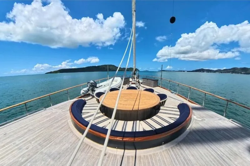 Odisea Yacht Photos Pics Custom Mahogany Gulet, 2006 model, with circular seating on deck, sailing in clear blue waters.