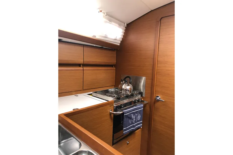  Yacht Photos Pics Interior of 2018 Jeanneau Sun Odyssey 419 yacht kitchen with stove and wooden cabinetry.