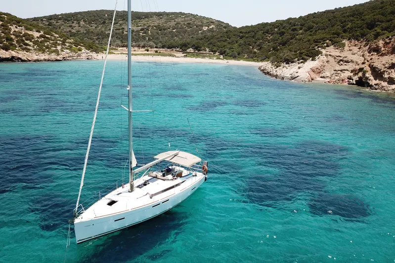  Yacht Photos Pics 2018 Jeanneau Sun Odyssey 419 sailboat anchored in clear turquoise waters near a rocky coastline.