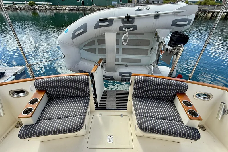 Tova Yacht Photos Pics 2007 Legacy Yachts 32 Sedan with seating and dinghy at the stern, docked by calm water.