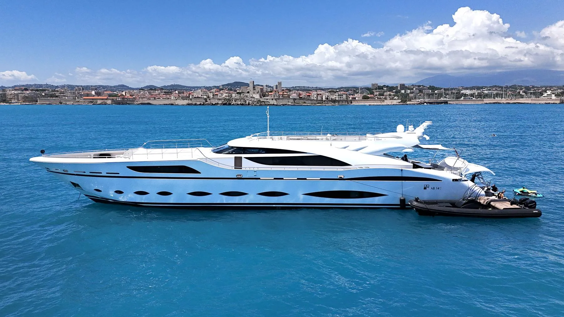 Luxurious 2016 AB Yachts model cruising on clear blue waters near a coastal city.