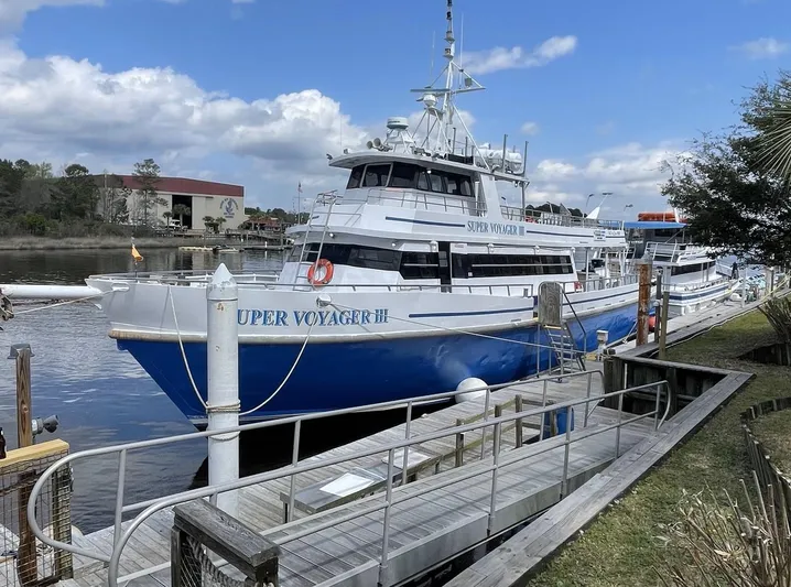 Super Voyager III Yacht Photos Pics Swiftships 1972 commercial passenger vessel docked by a wooden pier under a partly cloudy sky.