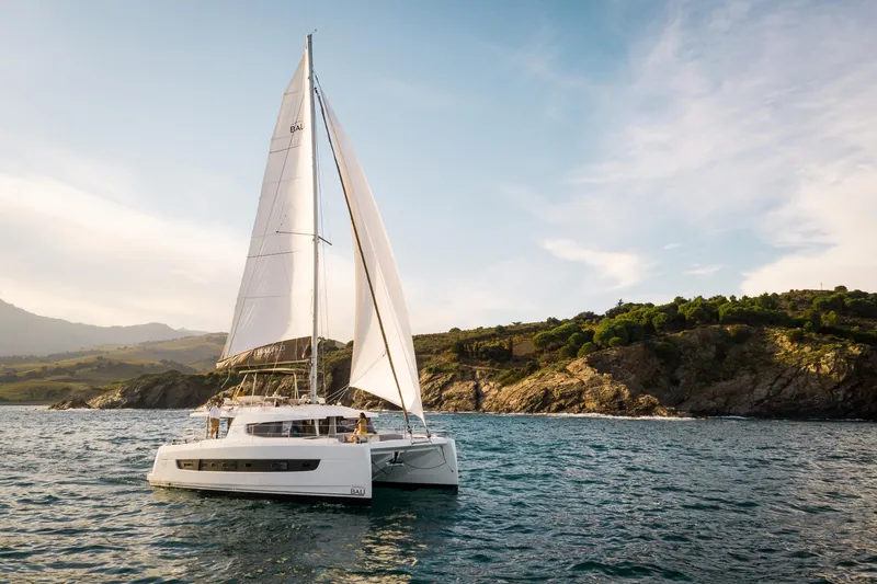 Azurea Yacht Photos Pics Sailing catamaran Bali 4.6 (2026) cruising near rocky coastline under clear skies.