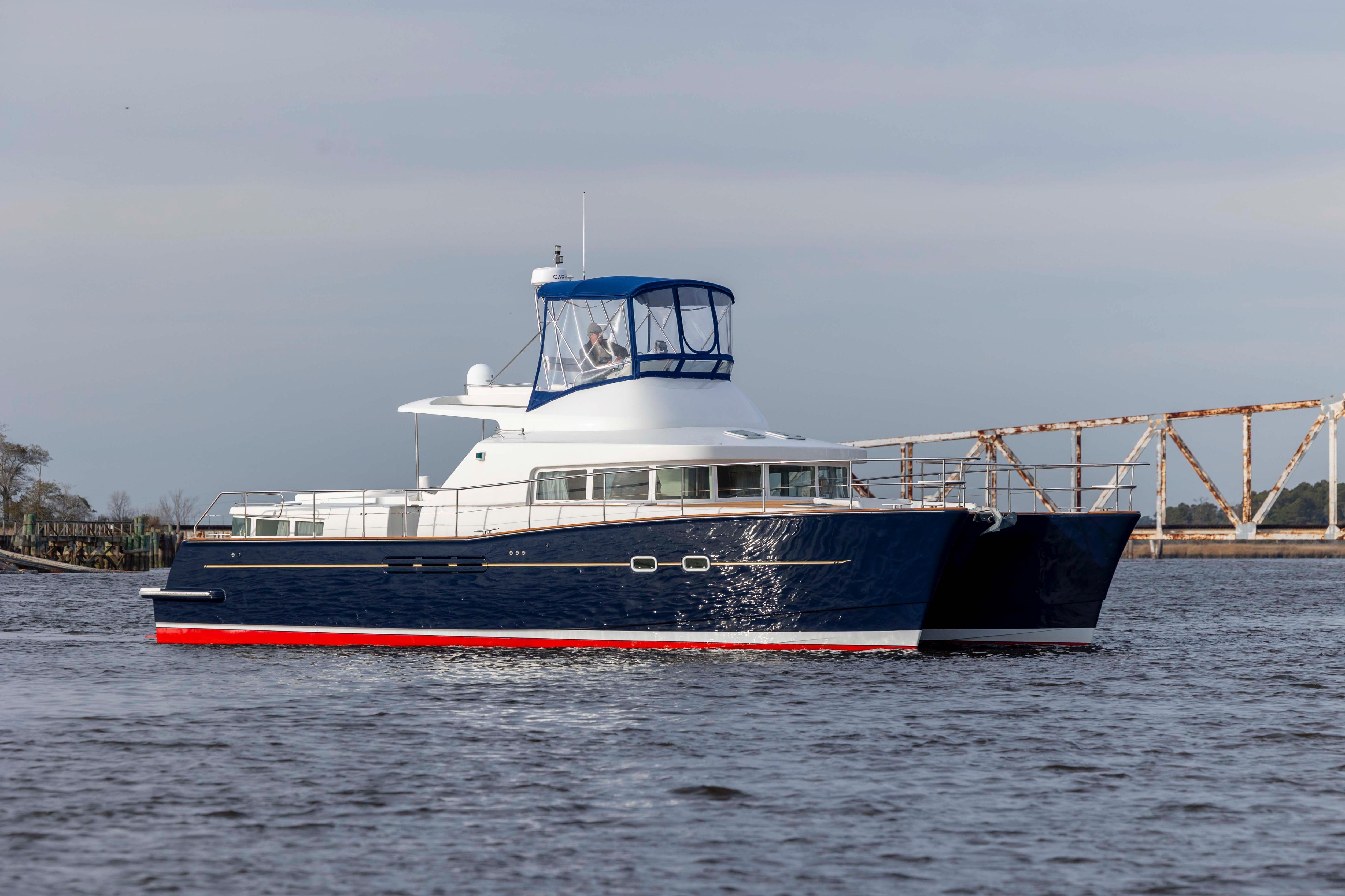 2004 Lagoon 43 PC yacht cruising on calm waters near a rusty bridge.