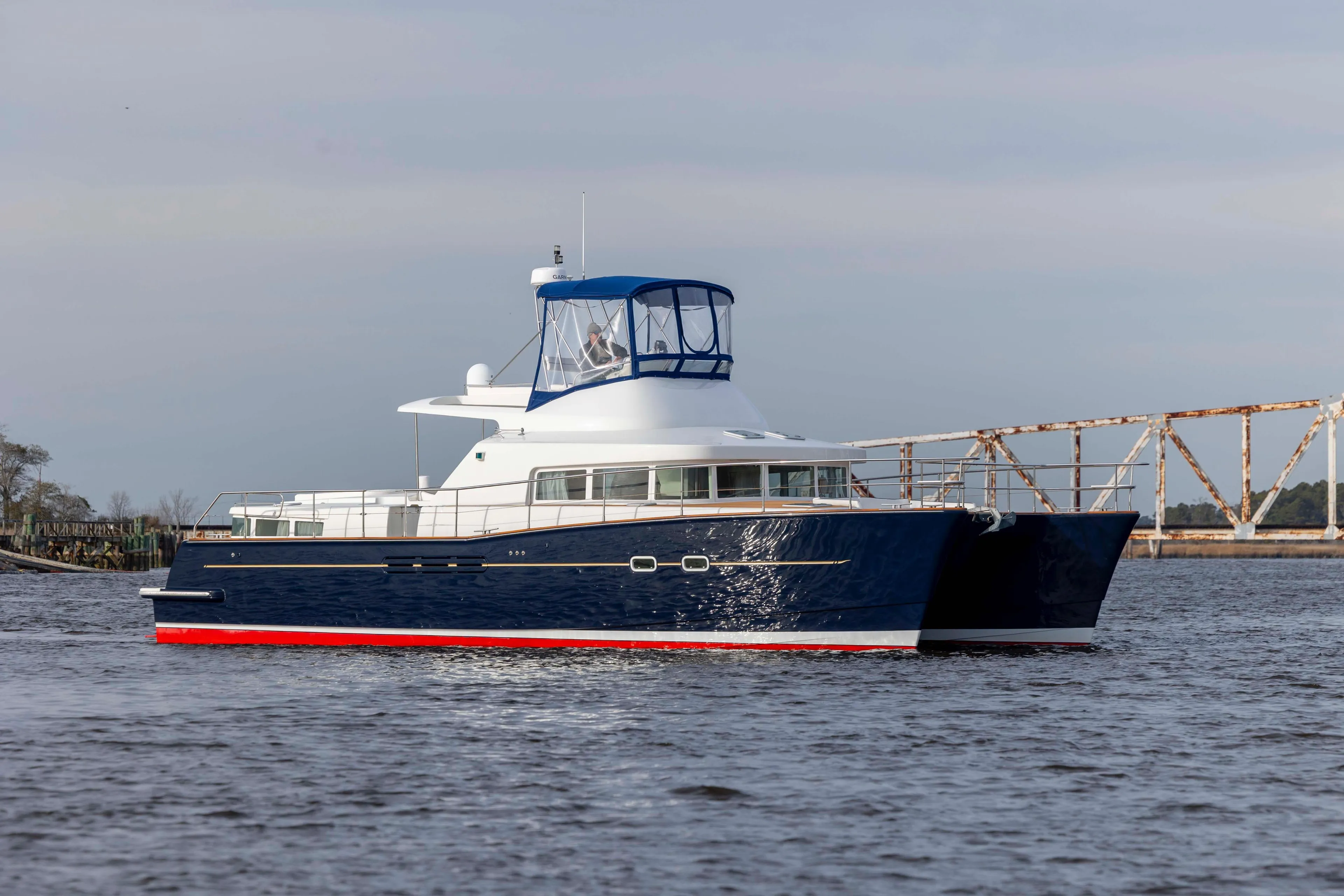 2004 Lagoon 43 PC yacht cruising on calm waters near a rusty bridge.
