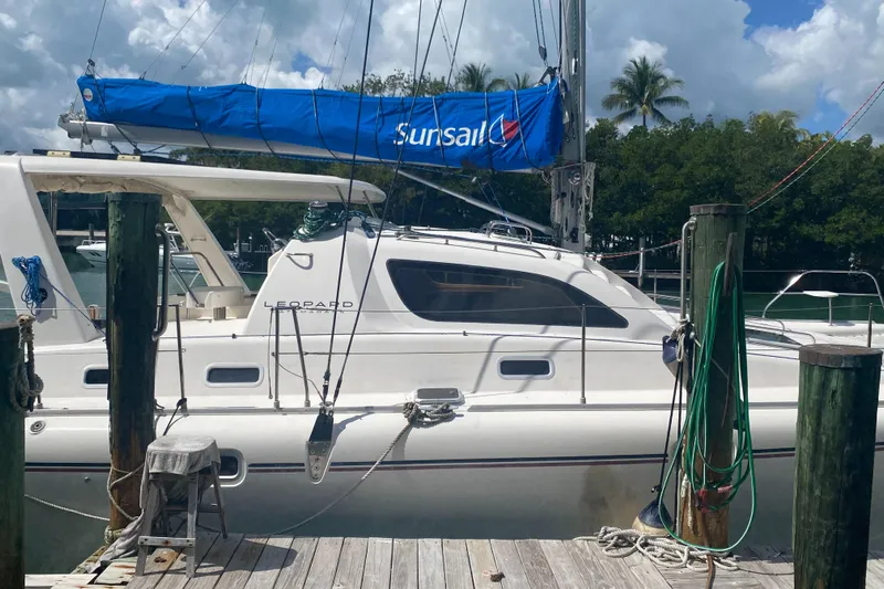 Tiki Yacht Photos Pics 2003 Leopard 38 catamaran docked, featuring a blue Sunsail cover and lush tropical backdrop.