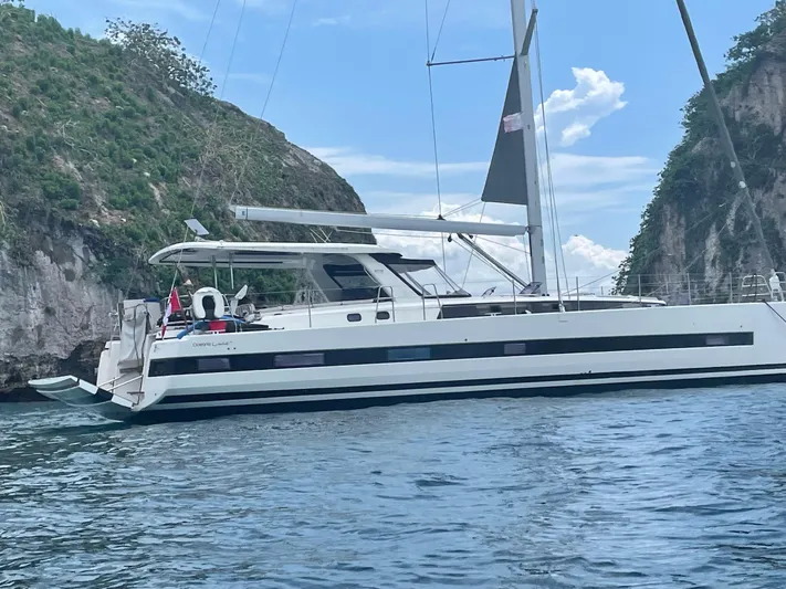 Gwint Yacht Photos Pics 2019 Beneteau Oceanis Yacht 62 sailing near rocky cliffs on a sunny day.