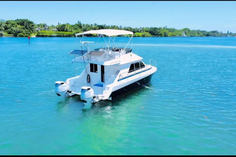  Yacht Photos Pics 2001 Zeta 32 Power Catamaran on clear blue water, lush green shoreline in background.