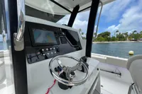 Steering console of 2022 Aquila Molokai 28 boat with navigation equipment, near scenic shoreline.