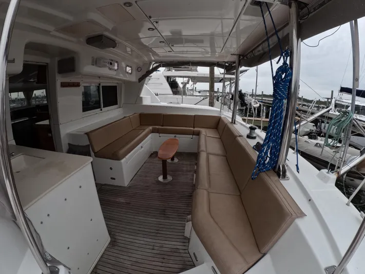 Orion Yacht Photos Pics Spacious seating area on a 2006 Lagoon 440 catamaran, featuring comfortable cushions and a wooden table.