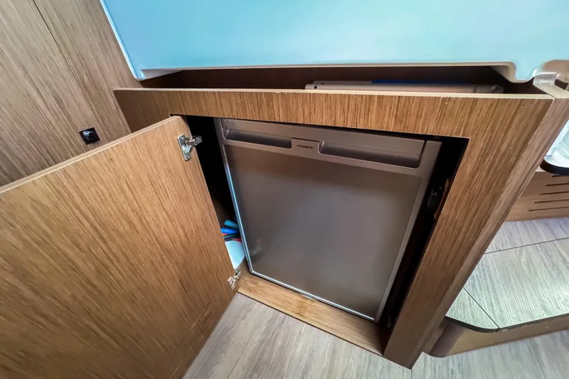  Yacht Photos Pics 2023 Beneteau Antares 11 interior with open wooden cabinet revealing a compact fridge.