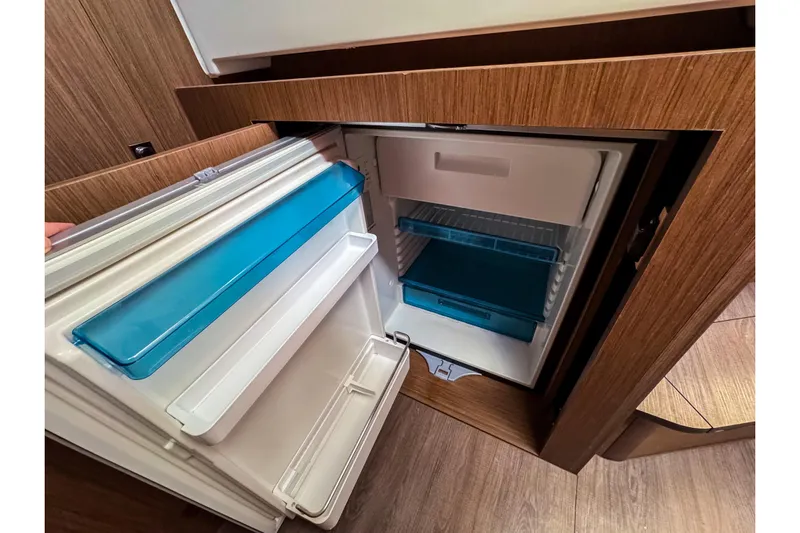  Yacht Photos Pics Open refrigerator inside 2023 Beneteau Antares 11 boat, featuring wooden cabinetry and modern design.