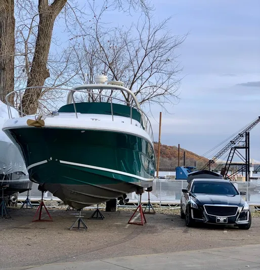 Serenity Yacht Photos Pics 2004 Sea Ray 340 Sundancer boat on stands beside a parked car, autumn trees in background.