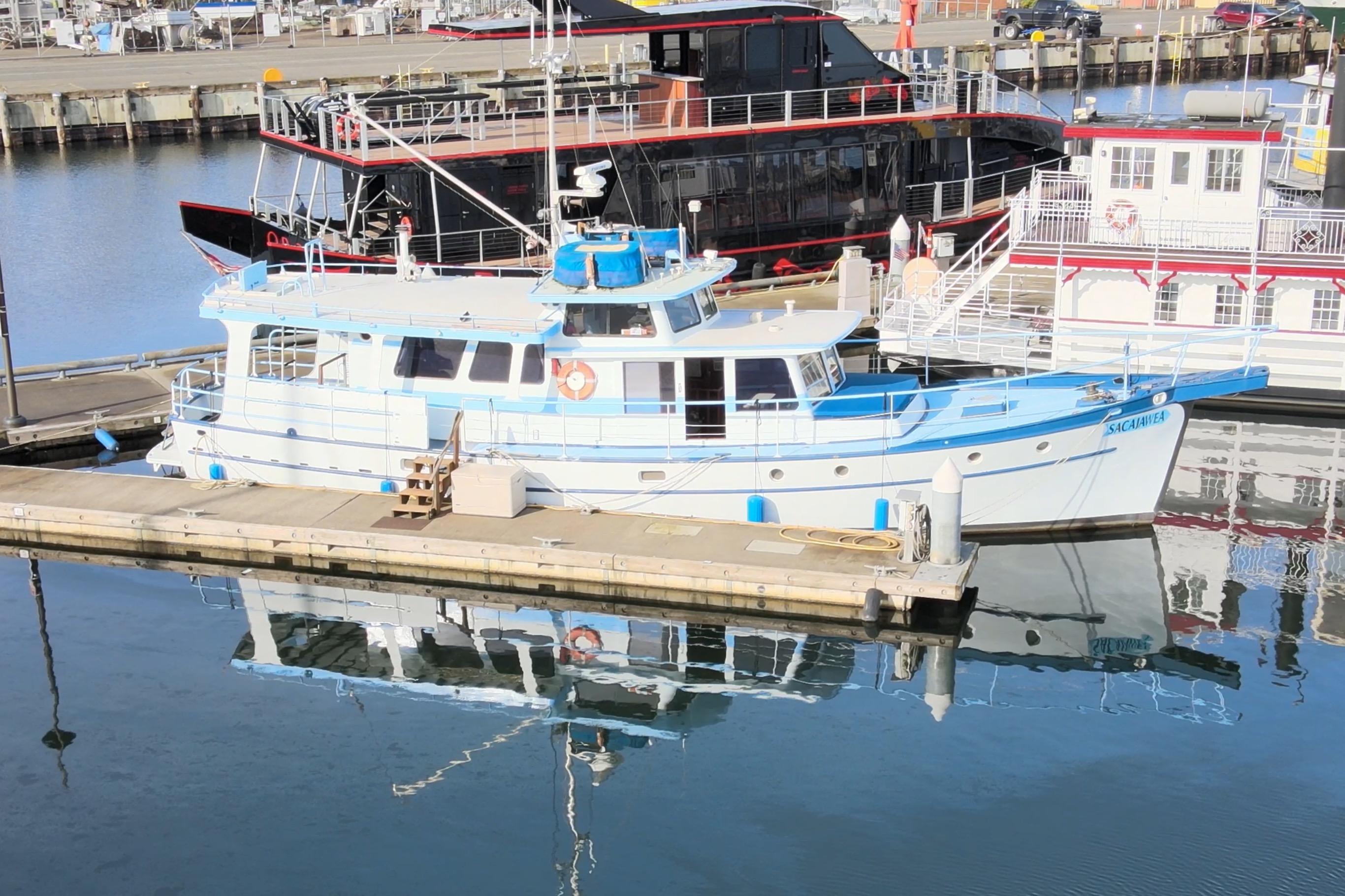 1965 Custom Trawler docked at marina, reflecting on calm water.