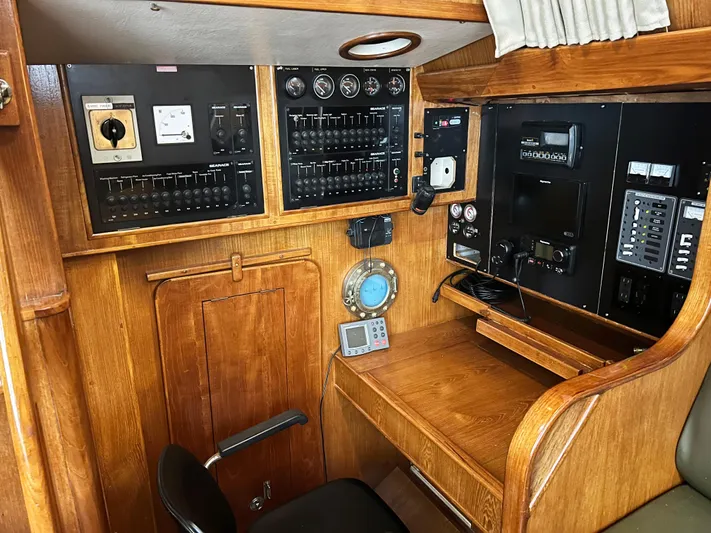 Here Be Dragons Yacht Photos Pics Navigation station of 1987 Oyster 46.5 yacht with control panels and wooden desk.