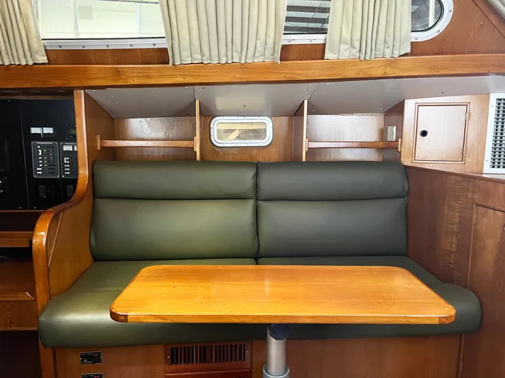 Here Be Dragons Yacht Photos Pics Interior of 1987 Oyster 46.5 yacht with green seating and wooden table.