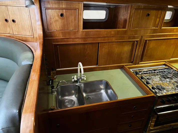 Here Be Dragons Yacht Photos Pics 1987 Oyster 46.5 yacht kitchen with wooden cabinets, double sink, and stove.