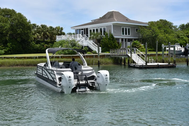  Yacht Photos Pics 2024 Bennington 27 QFB boat cruising near a waterfront house with lush greenery.