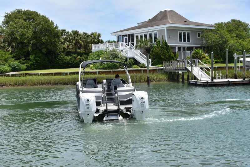  Yacht Photos Pics 2024 Bennington 27 QFB boat cruising near a waterfront house.
