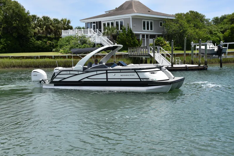 Yacht Photos Pics 2024 Bennington 27 QFB pontoon boat cruising near a waterfront house.