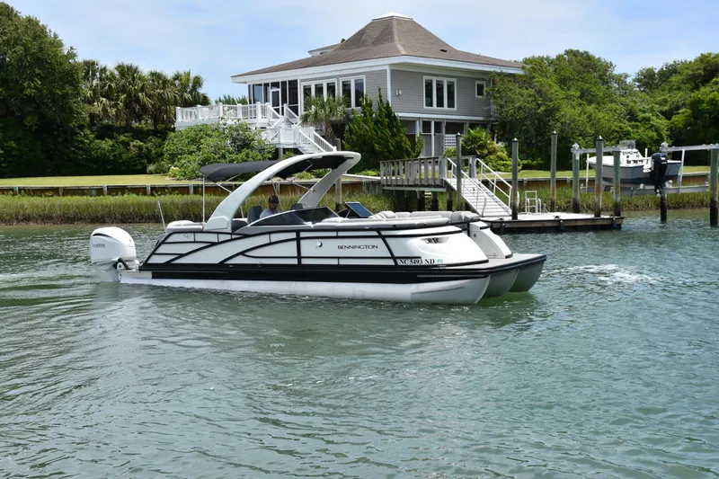  Yacht Photos Pics 2024 Bennington 27 QFB pontoon boat cruising near a waterfront house.