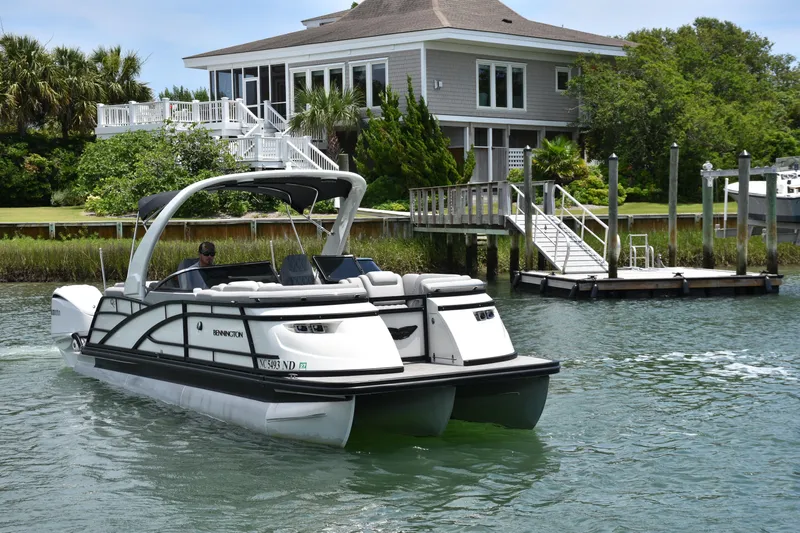  Yacht Photos Pics 2024 Bennington 27 QFB pontoon boat cruising near a waterfront house.
