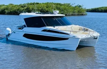  Yacht Photos Pics 2023 Aquila 36 Sport boat on calm water, surrounded by lush greenery.