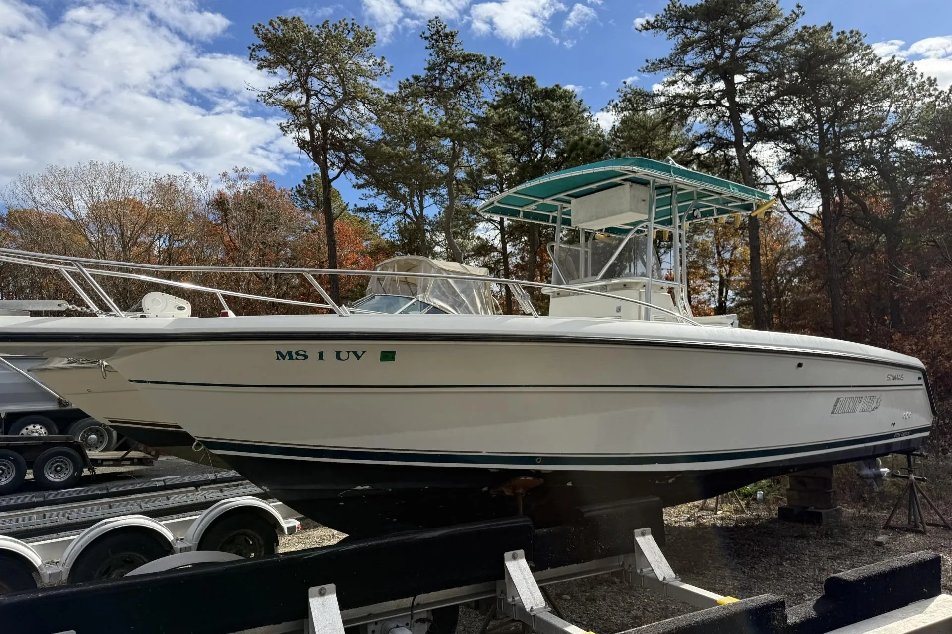 1997 Stamas 270 Tarpon boat on trailer, surrounded by trees under a partly cloudy sky.