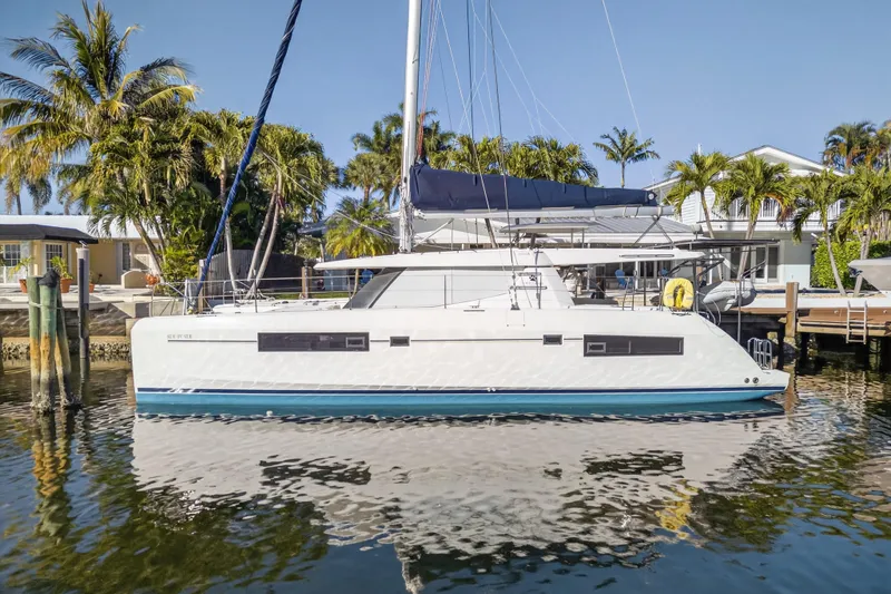  Yacht Photos Pics 2019 Leopard 45 catamaran docked by palm trees, reflecting on calm water.