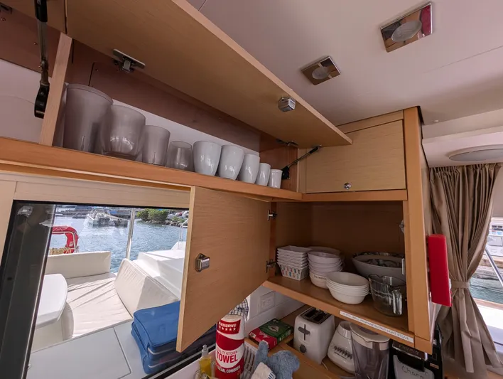 Southern Charm Yacht Photos Pics Interior of 2015 Lagoon 450 F yacht kitchen with open cabinets displaying dishes and mugs.