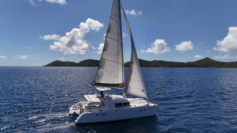 Southern Charm Yacht Photos Pics 2015 Lagoon 450 F catamaran sailing on open sea with scenic island backdrop.