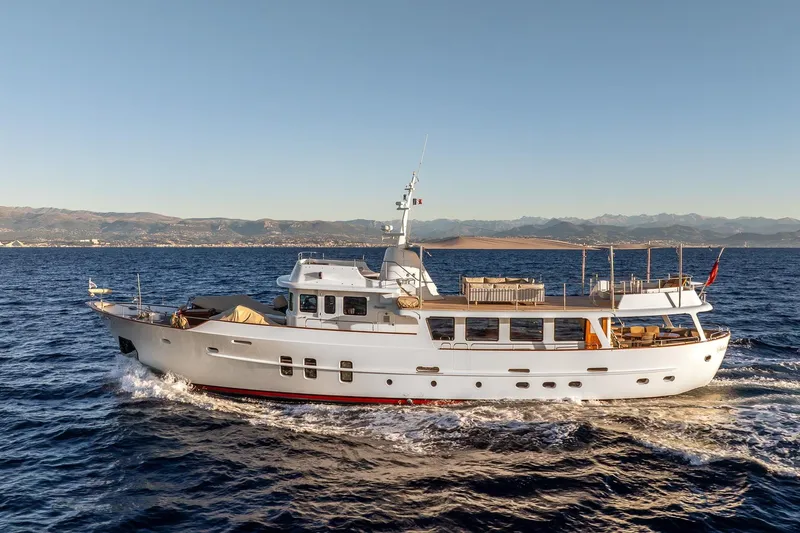 Sultana Yacht Photos Pics Classic 1969 Feadship 25.8m yacht cruising on open sea with scenic mountain backdrop.