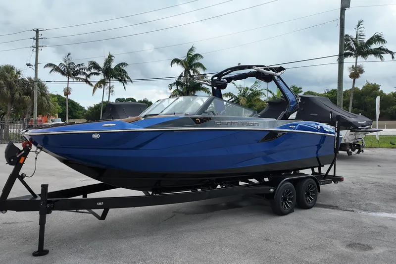  Yacht Photos Pics 2025 Centurion Fe23 boat in blue on trailer, parked outdoors with palm trees.