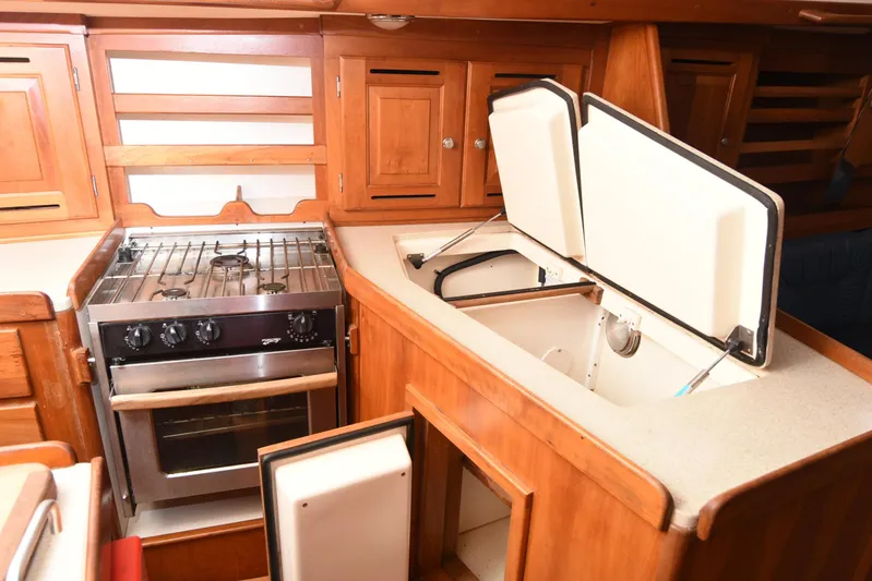 Makasi Yacht Photos Pics 2008 Tartan 4100 yacht kitchen with stove, wooden cabinets, and open storage compartments.