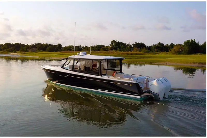 New Mjm 3 Yacht Photos Pics 2026 MJM 3 boat cruising on calm water near a grassy shoreline.