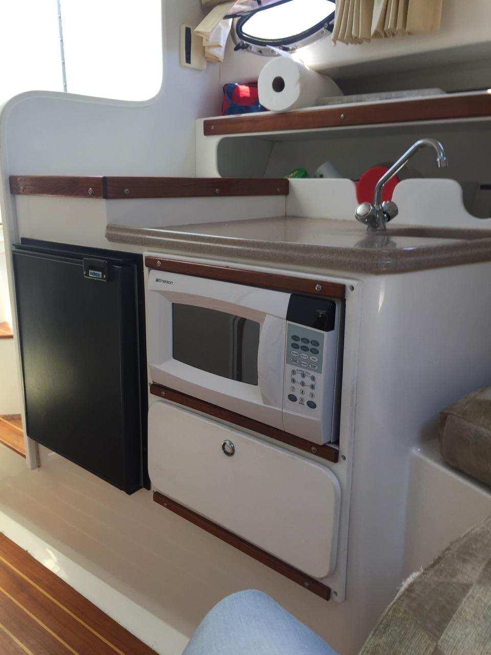 2004 Stamas 310 Express boat interior with kitchenette, featuring a microwave, sink, and mini-fridge.