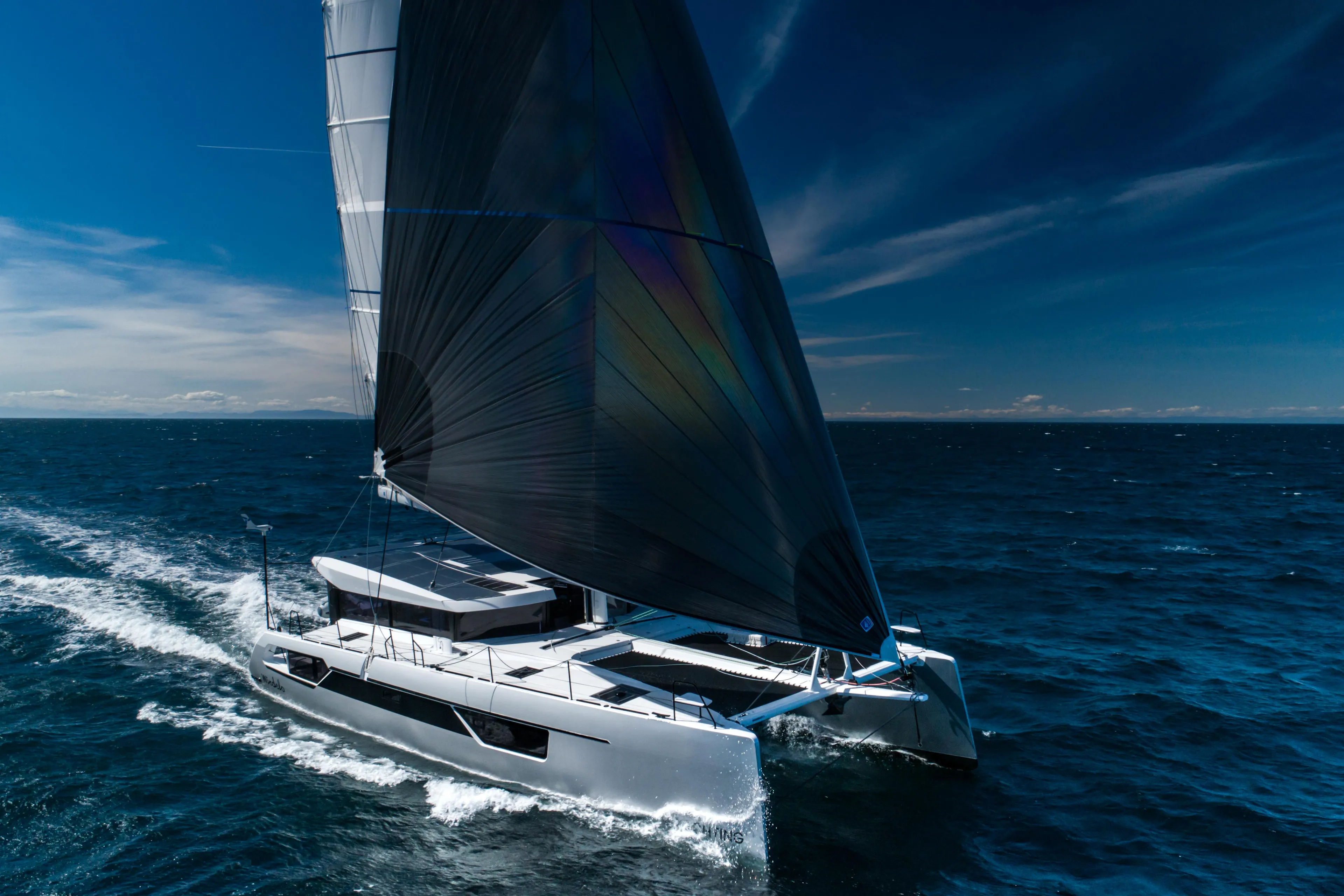 Windelo 54 sailing catamaran 2025 gliding on open ocean under clear blue sky.
