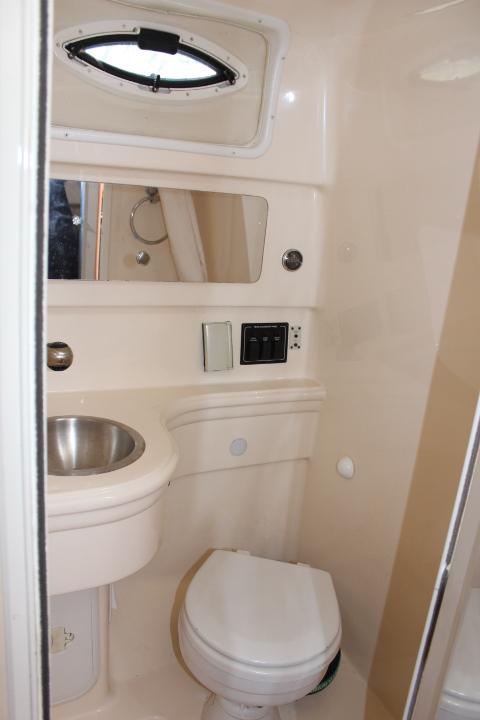 Compact bathroom in a 2005 Larson Cabrio 240 boat with sink, toilet, and mirror.