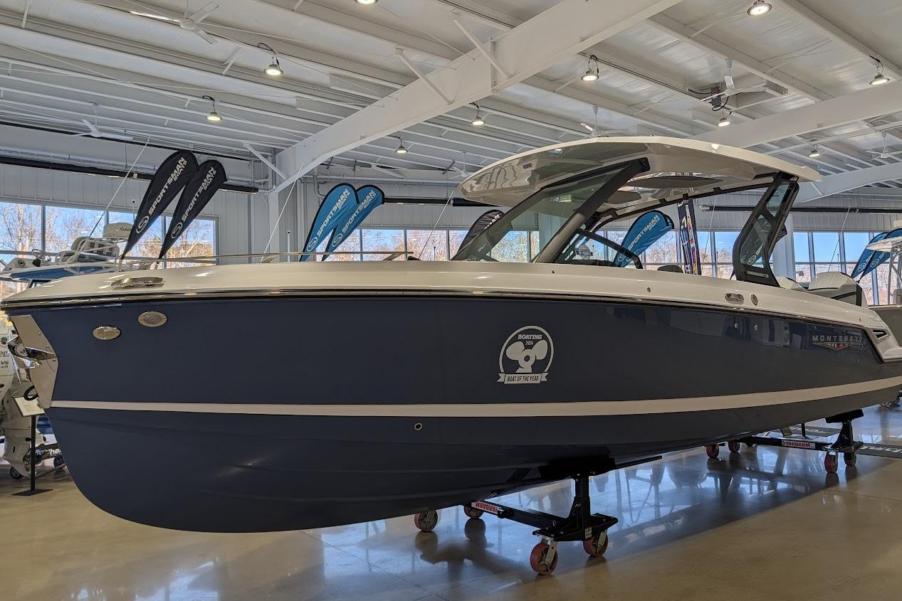 2026 Monterey Elite 30 OB boat displayed in a showroom with banners.