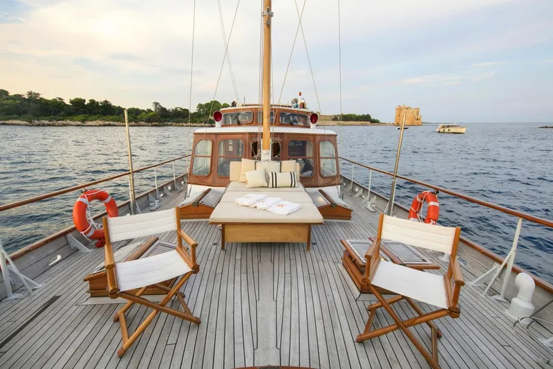 Atalanta J Yacht Photos Pics 1958 Feadship ATALANTA J yacht deck with chairs and table, overlooking serene waters.