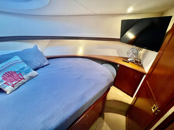 Open Time Yacht Photos Pics 2006 Silverton 34 Convertible yacht bedroom with TV, blue bedding, and wooden cabinetry.