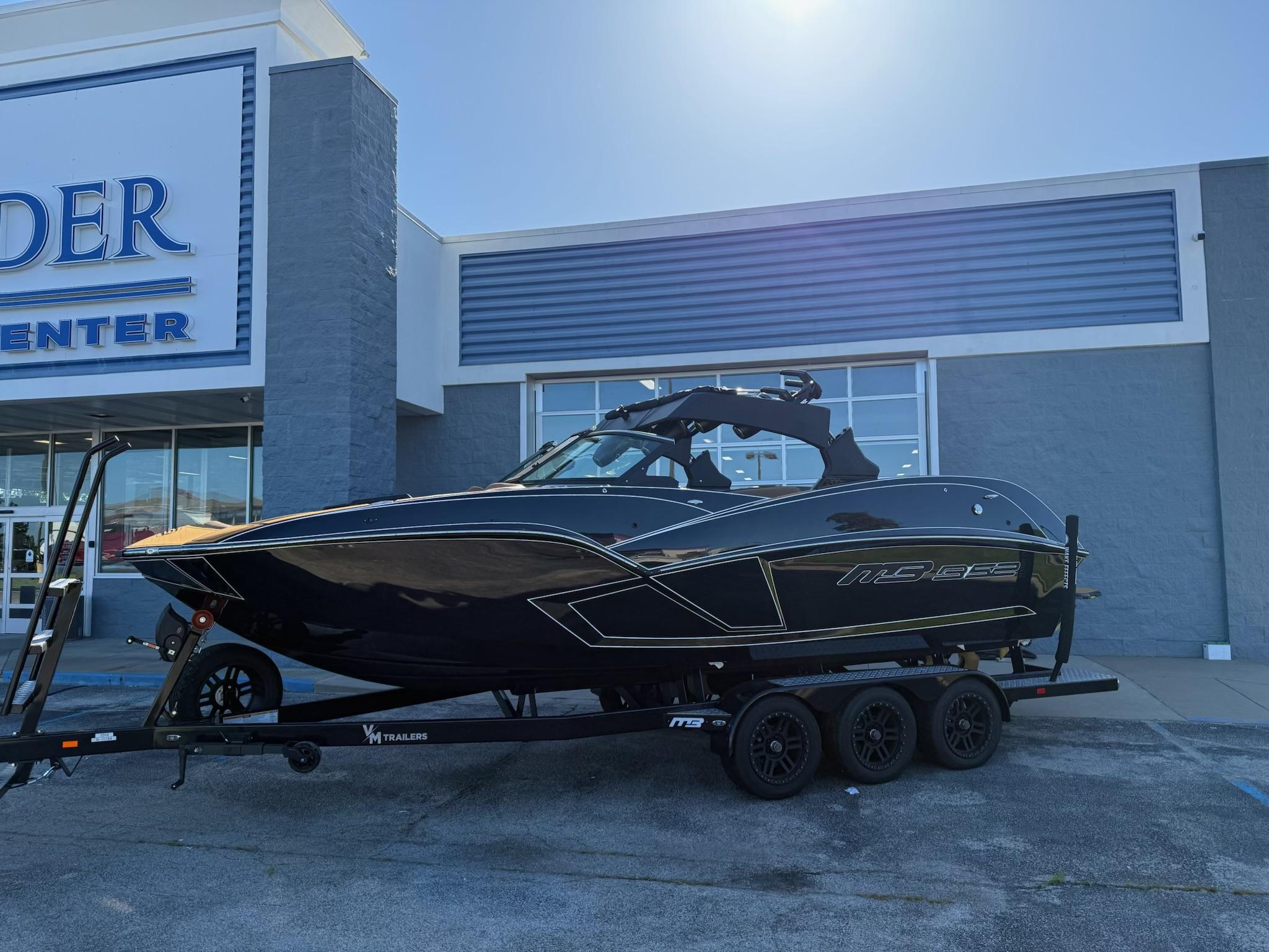 2025 MB B52 25 Alpha boat on trailer outside dealership, sleek black design.