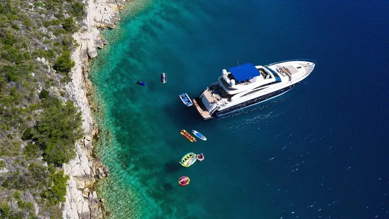  Yacht Photos Pics Luxurious Princess V85 yacht anchored near a scenic coastline, surrounded by clear blue water.