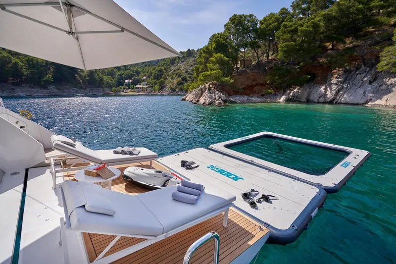  Yacht Photos Pics Luxurious Azimut Grande 27 METRI yacht deck with sun loungers, floating platform, and scenic coastal view.